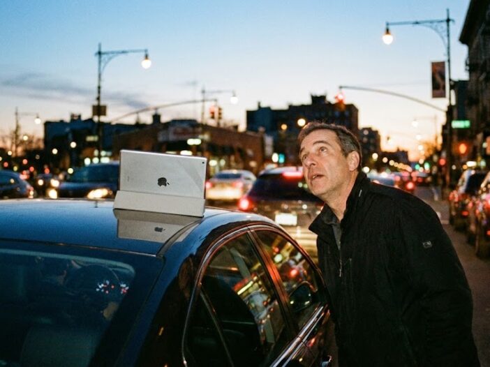 Hombre mirando con asombro un iPad olvidado en el techo de su coche al atardecer.